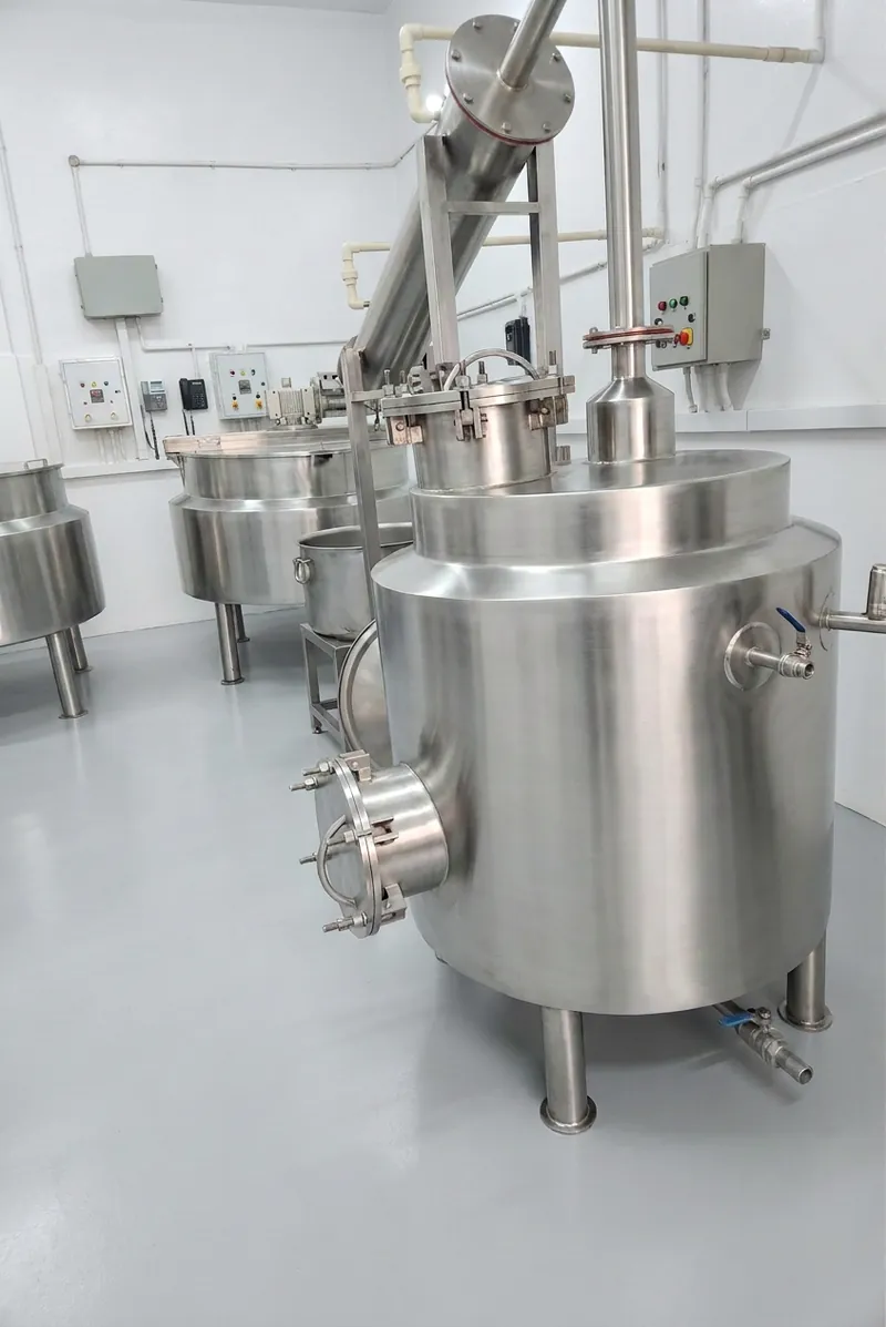 Prabhat's herbal arq distillation still in the foreground, with steam-jacketed kettles behind it, at our Amritsar factory